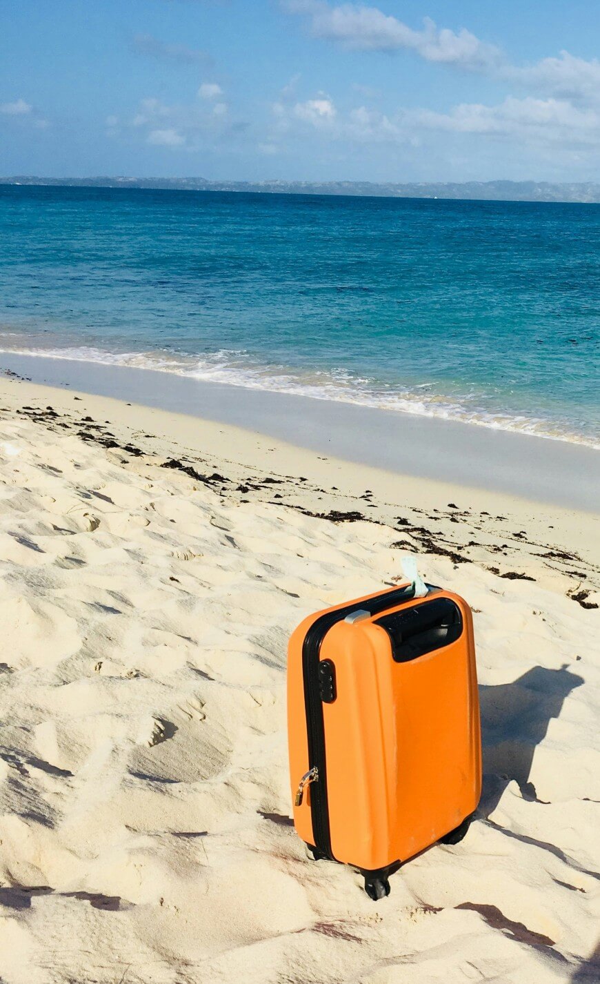orange suitcase on caribbean beach