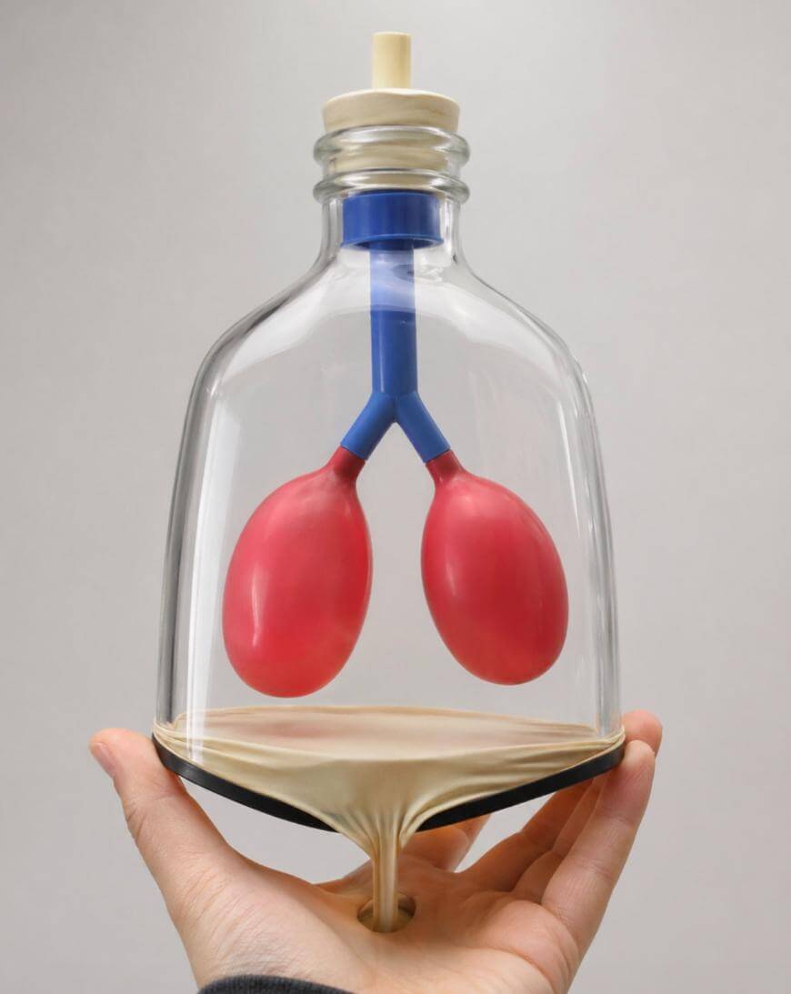 A hand holds a glass container shaped like an hourglass with red balloon-like structures inside, resembling lungs, connected by blue tubes; sand is flowing to the bottom chamber.