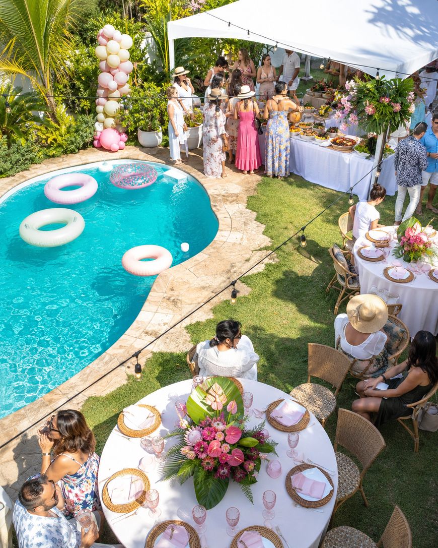 A backyard party with people gathered around tables and a buffet under a canopy. There’s a pool with colorful float rings, floral decorations, and a festive atmosphere. Some guests wear sun hats and summer clothes.