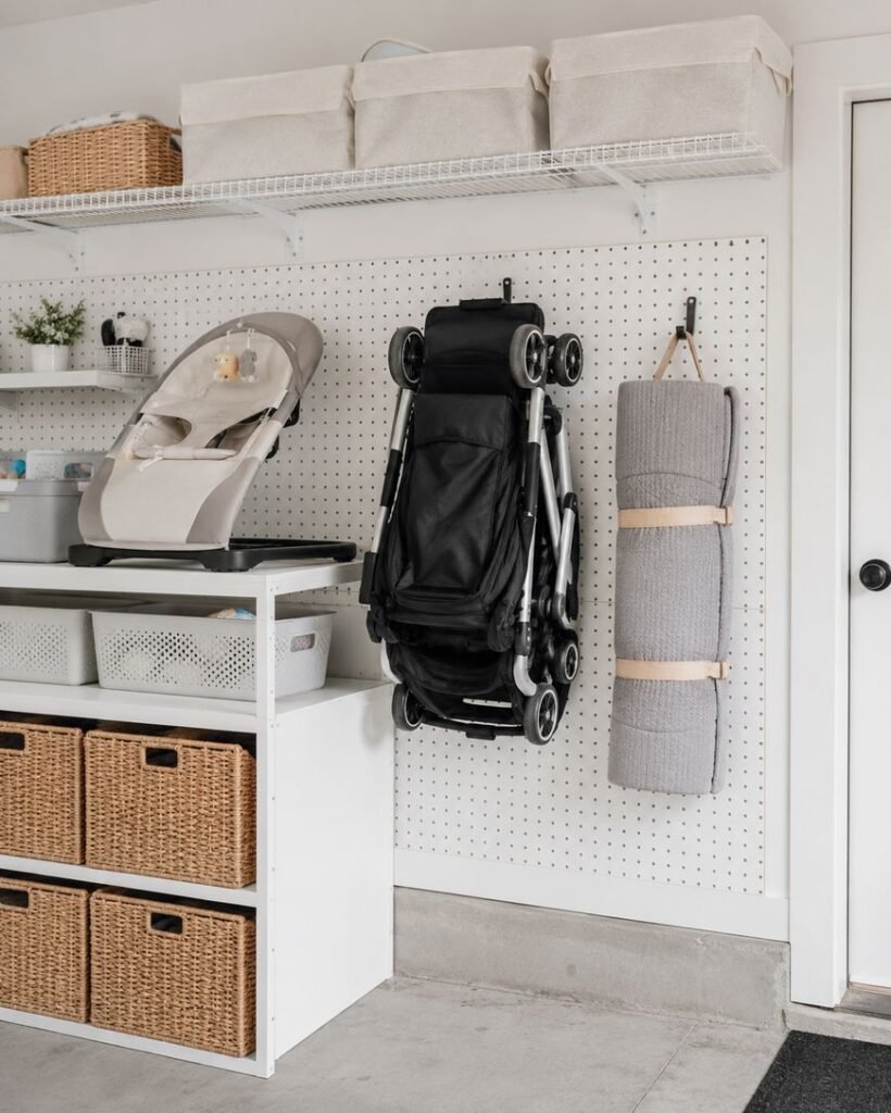 Organized storage area with baskets and bins on shelves, a folded stroller and rolled-up mat hanging on a pegboard, and a baby high chair on a countertop, all in a clean, modern room.