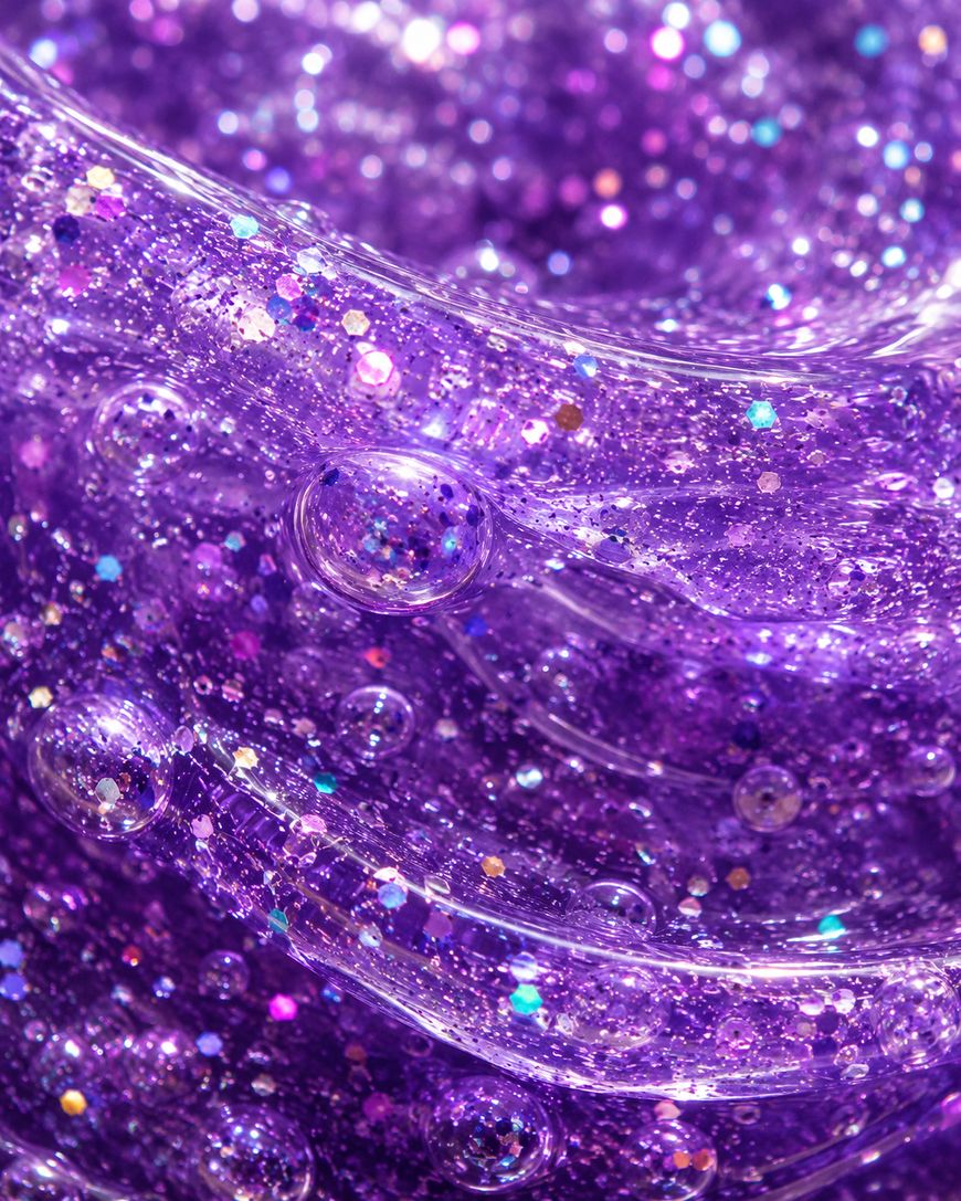 Close-up of clear purple slime with sparkling glitter and bubbles throughout, creating a shiny, textured, and colorful abstract appearance.