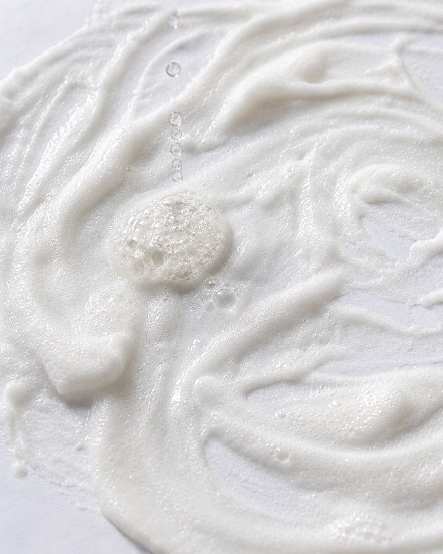 White foamy liquid with bubbles spread in swirling patterns across a smooth, white surface.