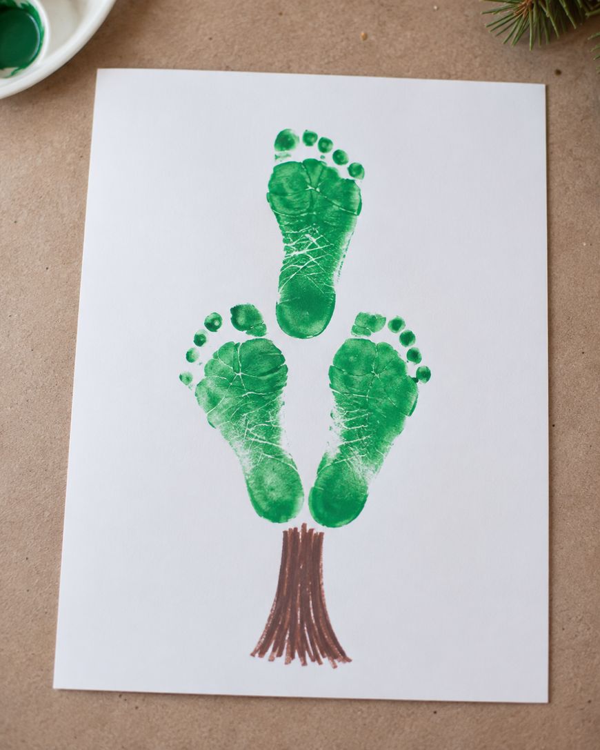 A white paper shows three green footprints arranged as leaves atop a brown trunk drawn with marker, resembling a tree.