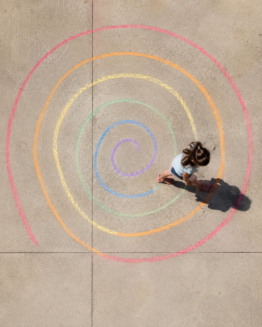 A child walks along a colorful spiral chalk drawing on concrete.