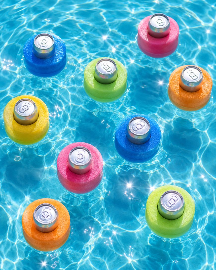 Nine soda cans in colorful foam holders float on clear blue pool water, creating ripples. Holders are pink, green, orange, yellow, and blue. Sunlight reflects off the water.
