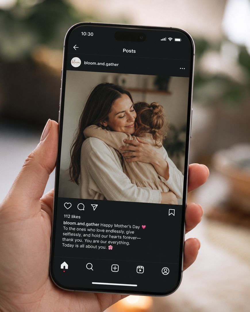 A hand holds a phone displaying an Instagram post of a woman hugging a child warmly, with a Happy Mothers Day message shown below the photo.
