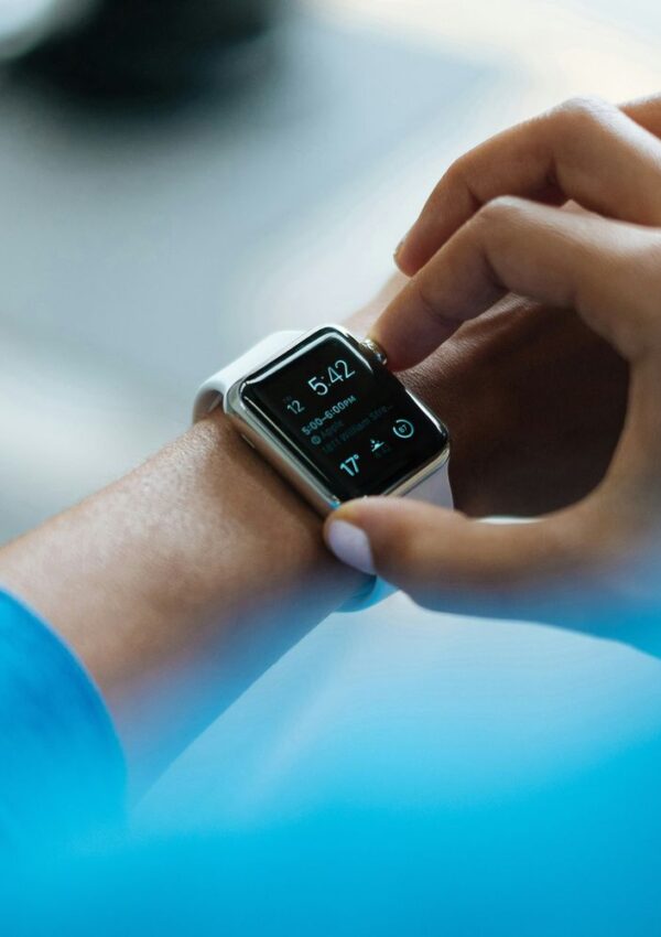 A person wearing a blue shirt interacts with a smartwatch displaying the time as 5:42. The watch screen also shows activity data. The hand is about to tap the screen.