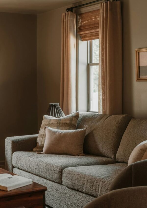 A textured sofa with several throw pillows sits in a cozy room, positioned next to a window with curtains.