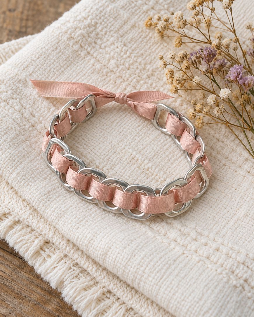 A bracelet made of silver-toned metal rings woven with light pink ribbon, tied in a small bow.